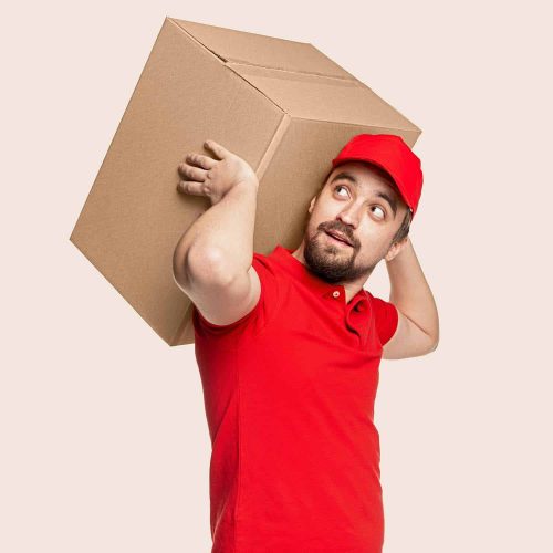 Adult bearded male courier in red uniform carrying heavy big carton package while delivering parcel against white background
